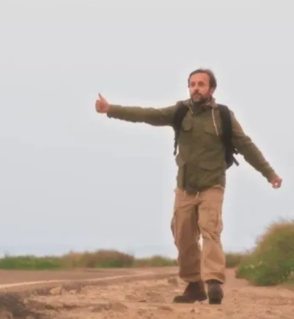 Người đàn ông đeo balo giơ ngón tay cái bắt xe đi quá độ trên đường (Hitchhiker travel)